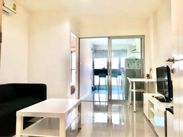 Bright modern living room with sleek furniture and glass partition leading to a cozy kitchen area.