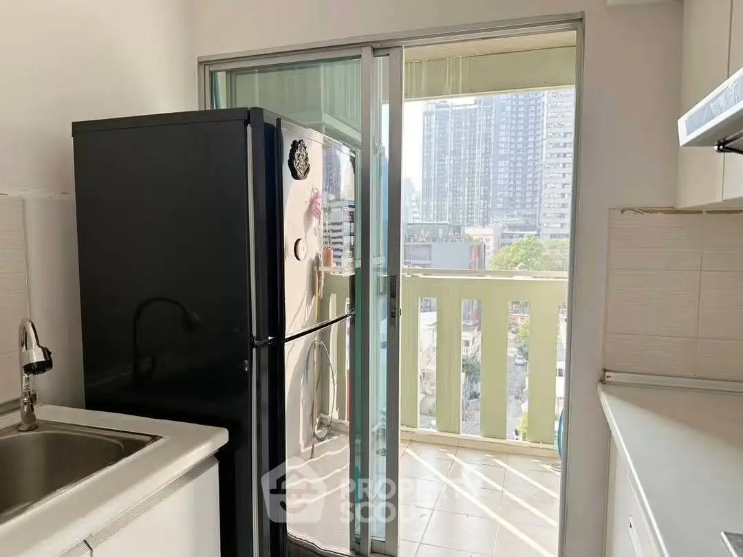 Modern kitchen with balcony view and sleek black fridge in urban apartment.