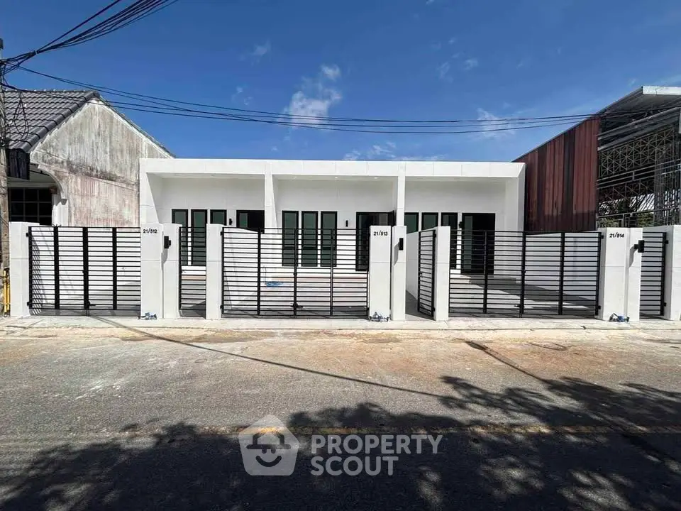 Modern townhouse exterior with sleek design and gated entrance under clear blue sky.