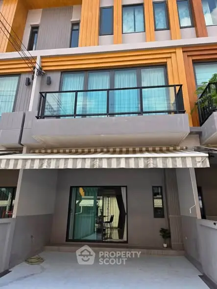 Modern townhouse exterior with large windows and balcony, featuring stylish wood paneling and a covered patio area.
