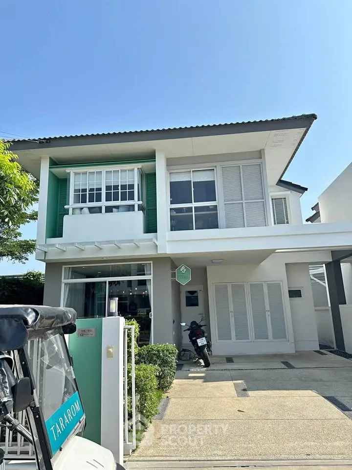 Modern two-story house with green accents and spacious driveway in sunny neighborhood.