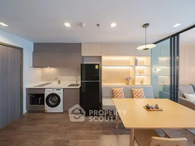 Modern open-plan living room with sleek kitchen and dining area, featuring stylish furniture and built-in appliances.
