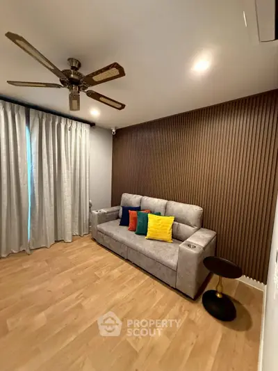 Modern living room with stylish sofa, wooden flooring, and ceiling fan, perfect for cozy relaxation.
