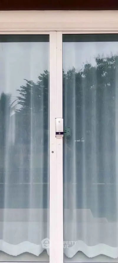 Modern sliding glass door with curtains offering a glimpse of outdoor greenery, perfect for natural light.