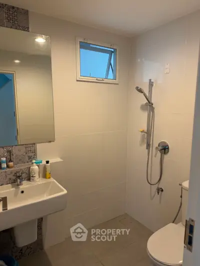 Modern bathroom with sleek fixtures and neutral tiles, featuring a shower and a small window for natural light.