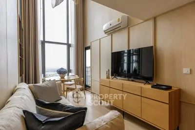 Modern living room with high ceilings and large windows, featuring stylish furniture and a cozy atmosphere.