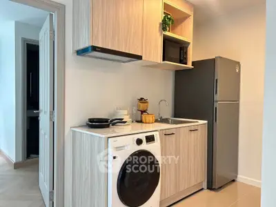 Modern compact kitchen with washing machine and stainless steel fridge in cozy apartment.