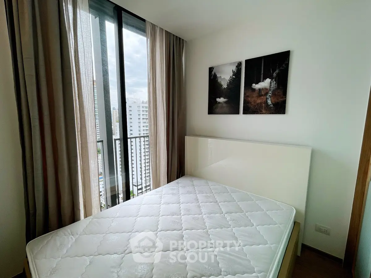 Modern bedroom with large windows and city view, featuring elegant decor and natural light.