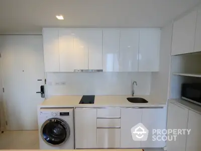 Modern kitchen with sleek white cabinets and built-in appliances including washing machine and stovetop.