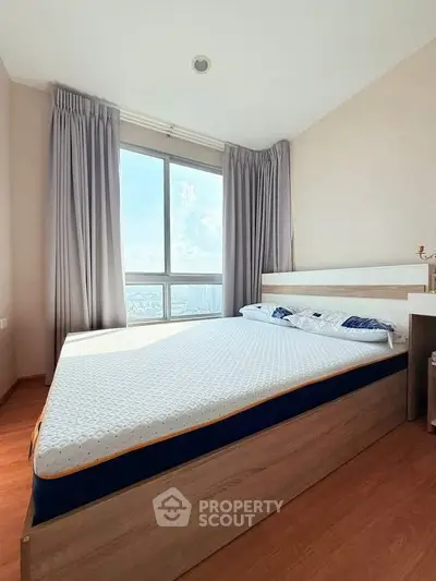 Bright bedroom with large window and modern bed frame, offering a stunning city view.
