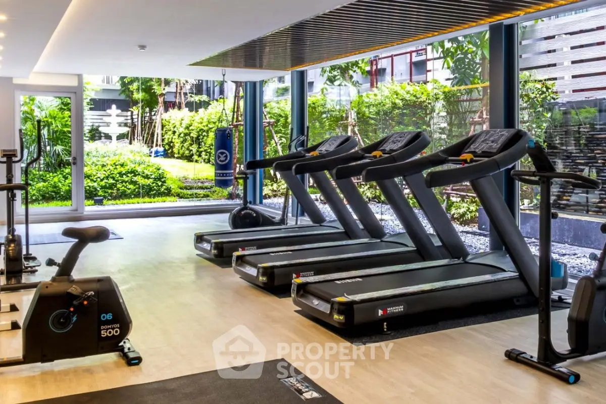 Modern gym with treadmills and exercise equipment overlooking lush garden view.