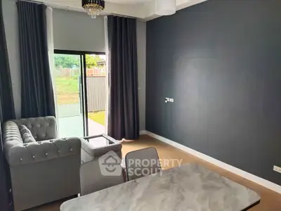 Modern living room with elegant gray sofa and dining table, featuring large window and stylish decor.