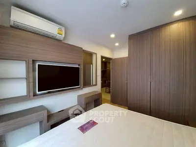 Modern bedroom with built-in wardrobe and wall-mounted TV in stylish apartment.