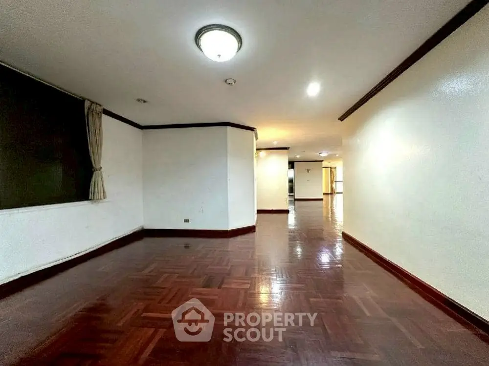 Spacious empty living room with polished wooden floors and bright lighting.