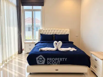 Elegant bedroom with plush bed and swan towel decor, featuring large windows and natural light.
