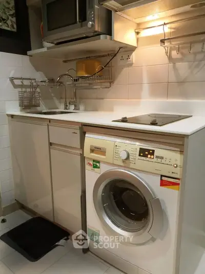 Compact kitchen with modern appliances including washing machine and microwave, ideal for urban living.