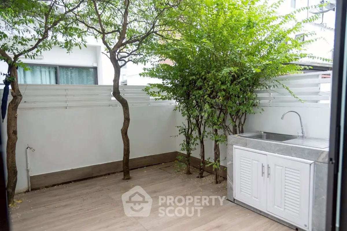 Charming outdoor patio with lush greenery and modern sink, perfect for relaxation and entertaining.