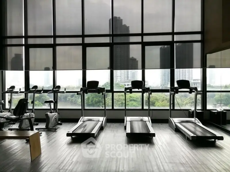 Spacious gym with modern equipment and city view, ideal for fitness enthusiasts.