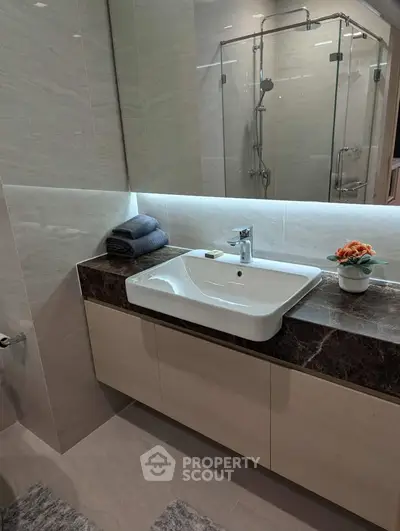 Modern bathroom with sleek sink and glass shower enclosure, featuring elegant marble countertop and stylish decor.