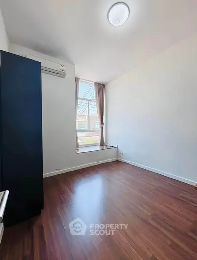 Bright empty room with wooden flooring and large window, perfect for customization.