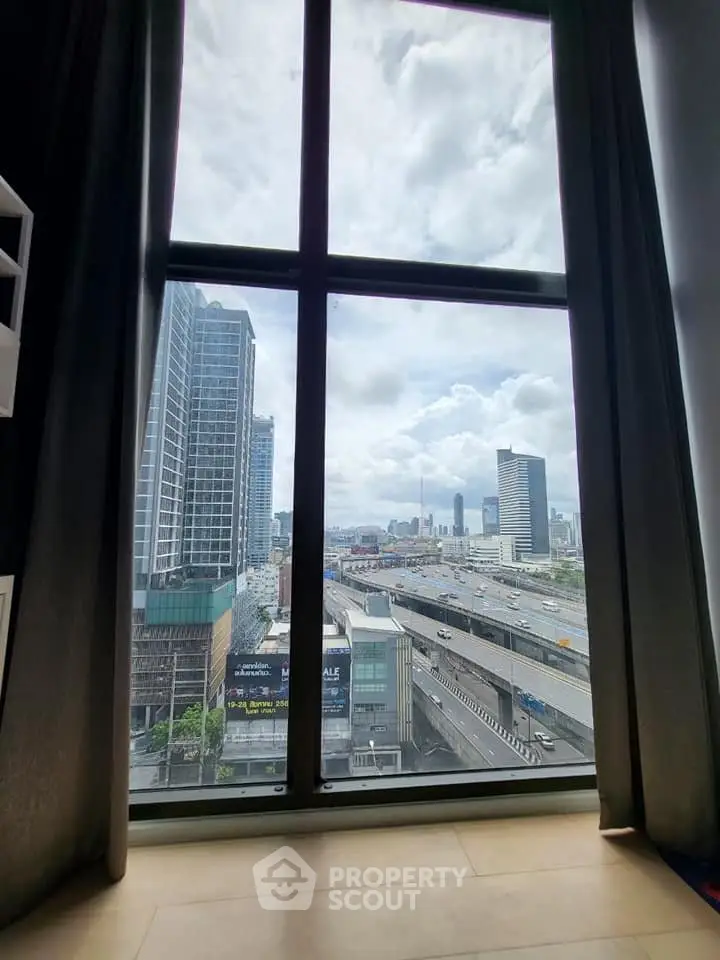 Stunning cityscape view from high-rise apartment window, showcasing urban skyline and highway.