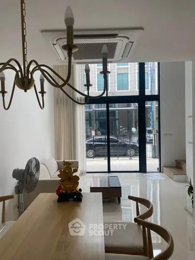 Modern living room with large windows, elegant chandelier, and stylish furniture in a bright, open space.