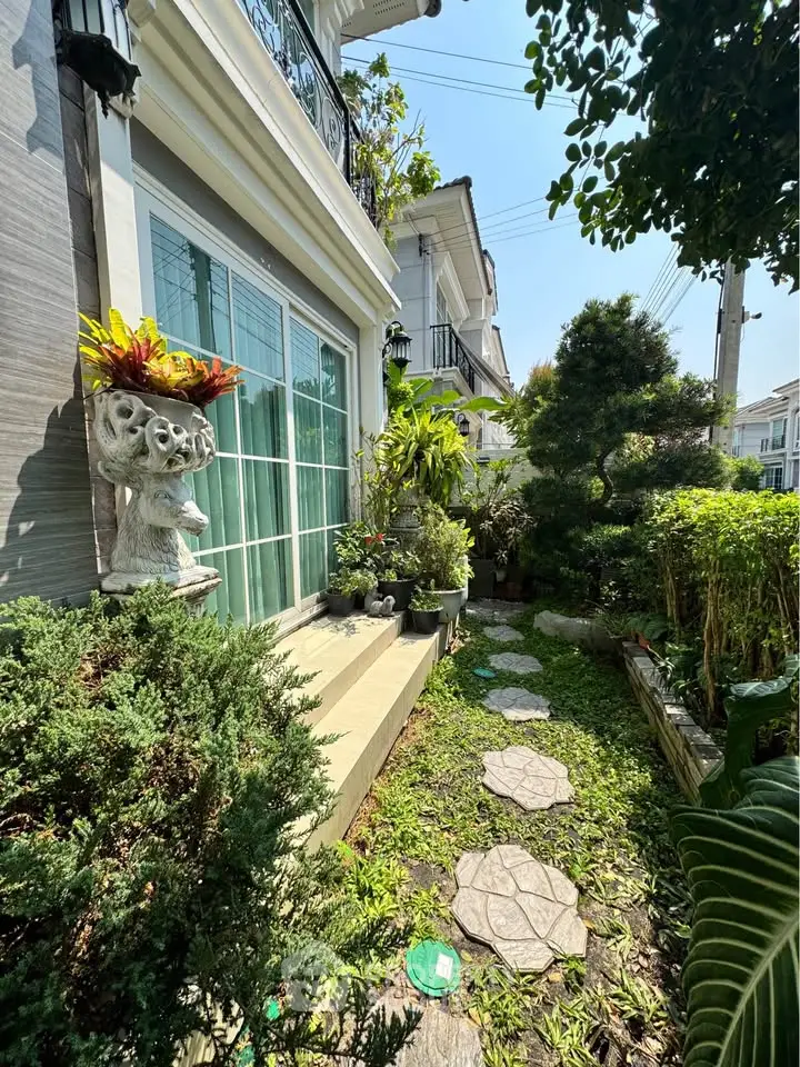 Charming garden path leading to a modern home's glass doors, surrounded by lush greenery and decorative plants.