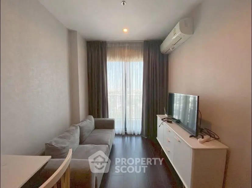 Cozy living room with modern sofa and TV, featuring natural light from large window.