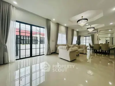 Spacious and elegant living room with chandeliers and large windows in a luxurious home.