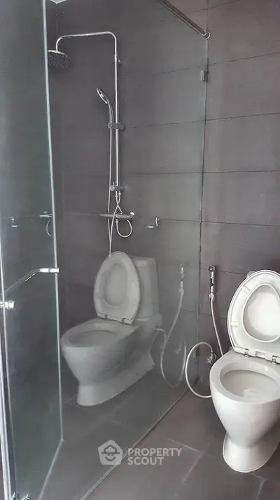 Modern bathroom with glass shower and dual toilets in sleek design.