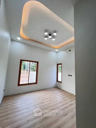 Modern empty room with stylish ceiling lights and wooden flooring, featuring large windows for natural light.