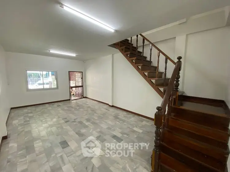Spacious living room with marble flooring and wooden staircase in modern home.