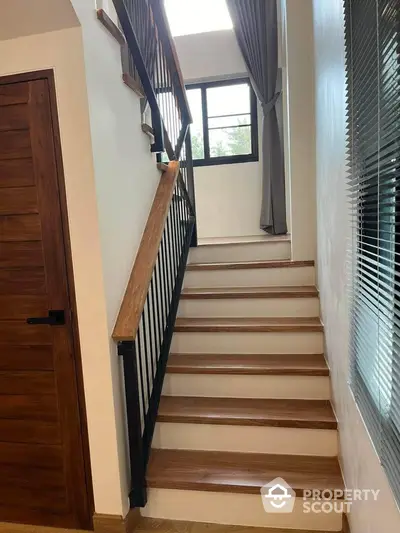 Elegant staircase with wooden steps and wrought-iron balusters, complemented by natural light from a window with stylish curtains.