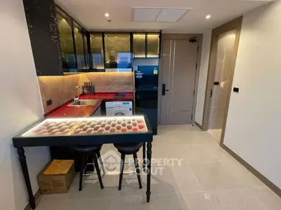 Modern kitchen with sleek black cabinets and red countertops, featuring a washing machine and stylish bar seating.