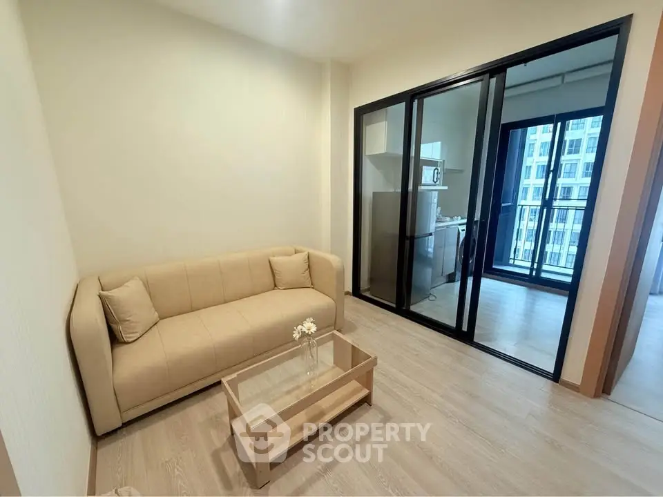 Modern living room with beige sofa and glass coffee table, adjacent to a balcony with city view.