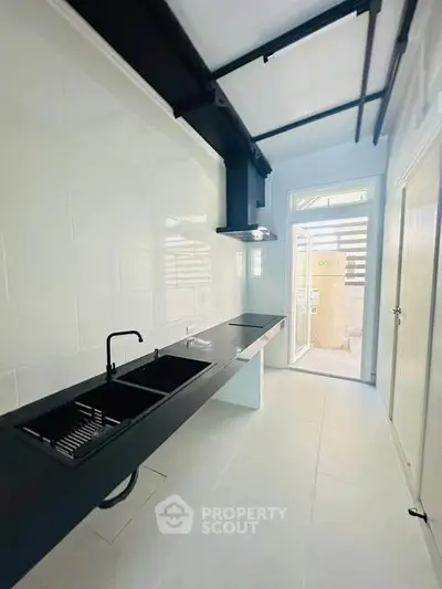 Sleek modern kitchen with black countertops and open layout, featuring a stylish sink and ample natural light.
