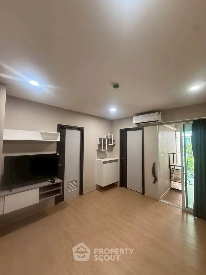 Modern living room with sleek design and balcony access, featuring built-in TV unit and air conditioning.