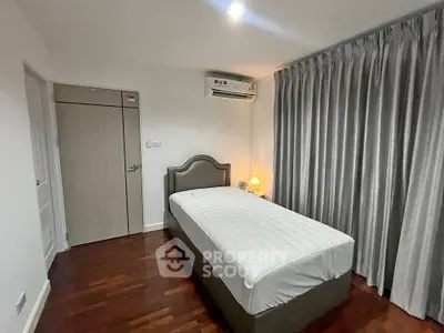 Cozy bedroom with single bed, elegant curtains, and warm lighting on wooden flooring.