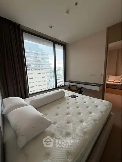 Modern bedroom with large window offering city view, featuring a comfortable bed and sleek desk.