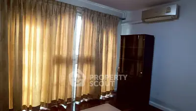 Cozy living room with large windows and elegant curtains, featuring a classic wooden cabinet and air conditioning.