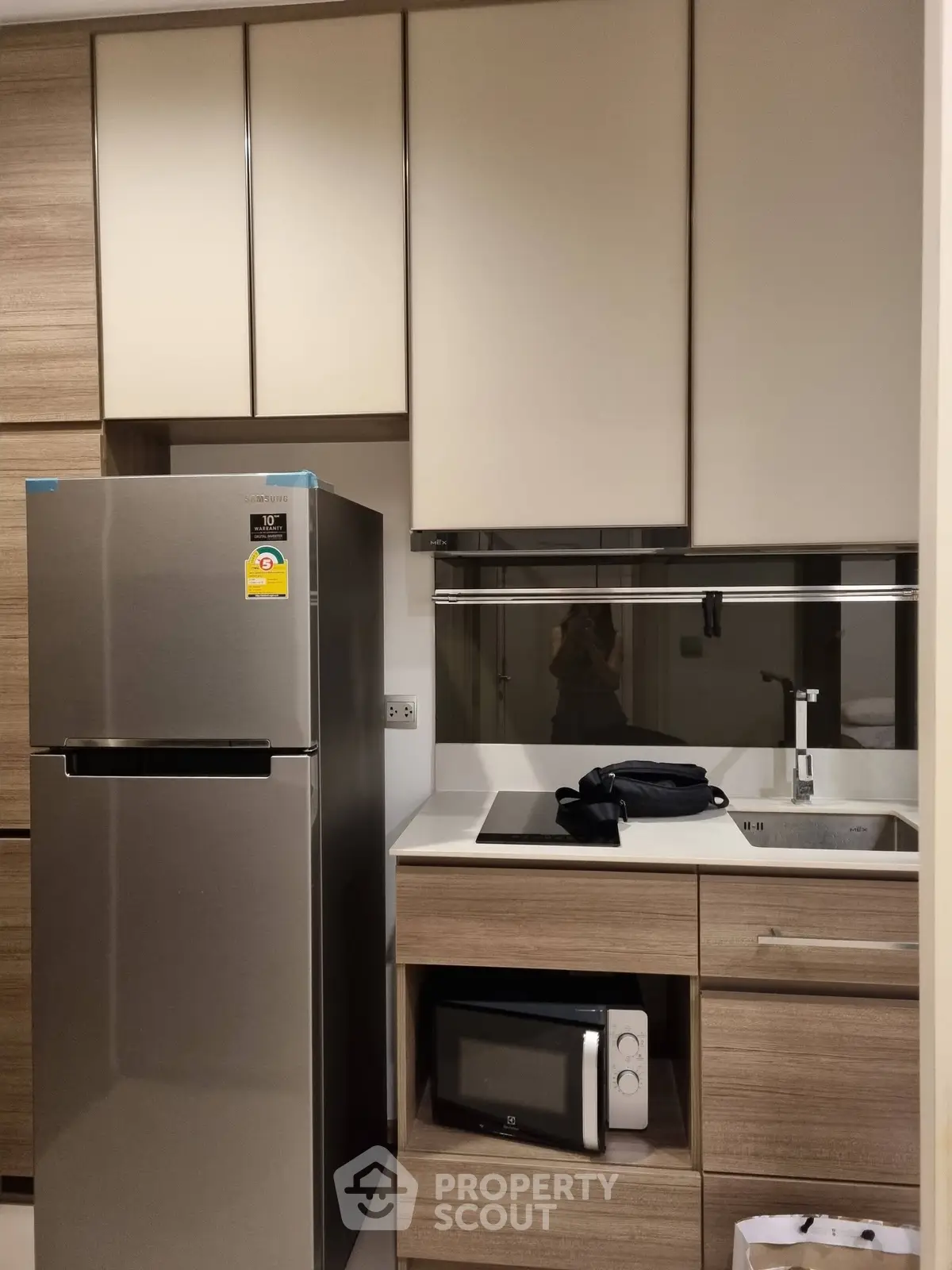 Modern kitchen with sleek cabinets, stainless steel fridge, and built-in microwave in a compact layout.