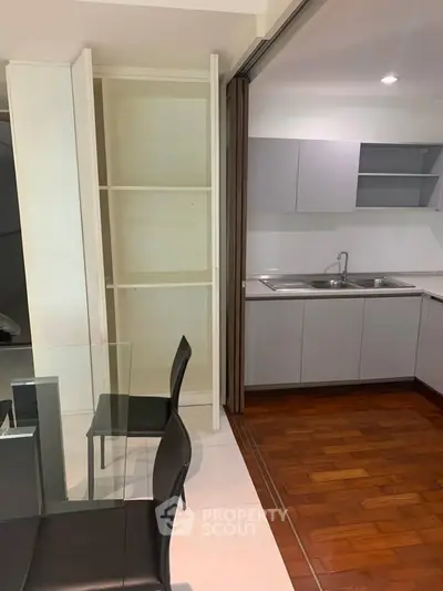 Modern kitchen with sleek cabinetry and dining area featuring glass table and black chairs.