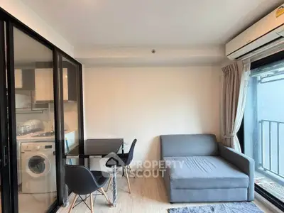 Modern living room with glass partition, sofa, dining table, and washing machine in compact space.
