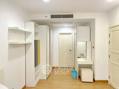 Spacious bedroom with modern white furniture and wooden flooring, featuring ample storage and a sleek vanity area.