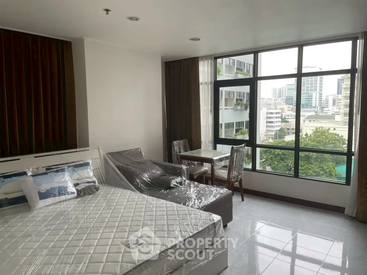 Spacious bedroom with large windows offering a stunning city view, featuring modern furniture and elegant decor.
