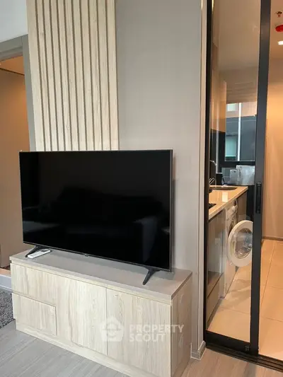 Modern living room with sleek TV setup and adjacent laundry area in stylish apartment.