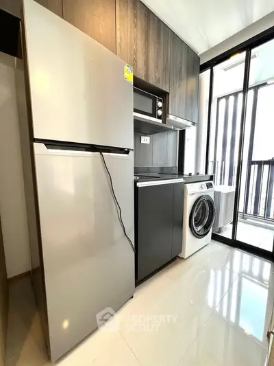 Modern kitchen with sleek appliances and natural light, featuring a fridge, microwave, and washing machine.