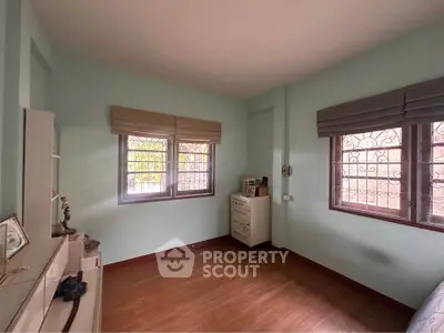 Cozy bedroom with wooden flooring and ample natural light from two windows.
