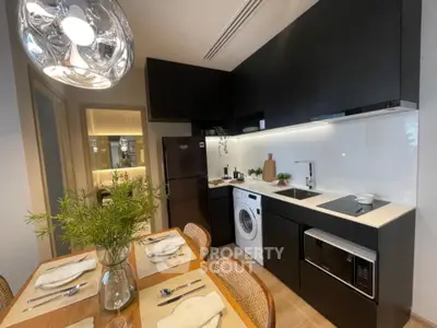 Modern kitchen with sleek black cabinetry and high-end appliances, including a built-in oven and washing machine, complemented by a stylish dining area.