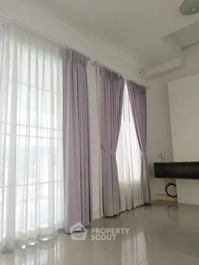 Spacious living room with elegant floor-to-ceiling curtains and glossy tiled flooring.